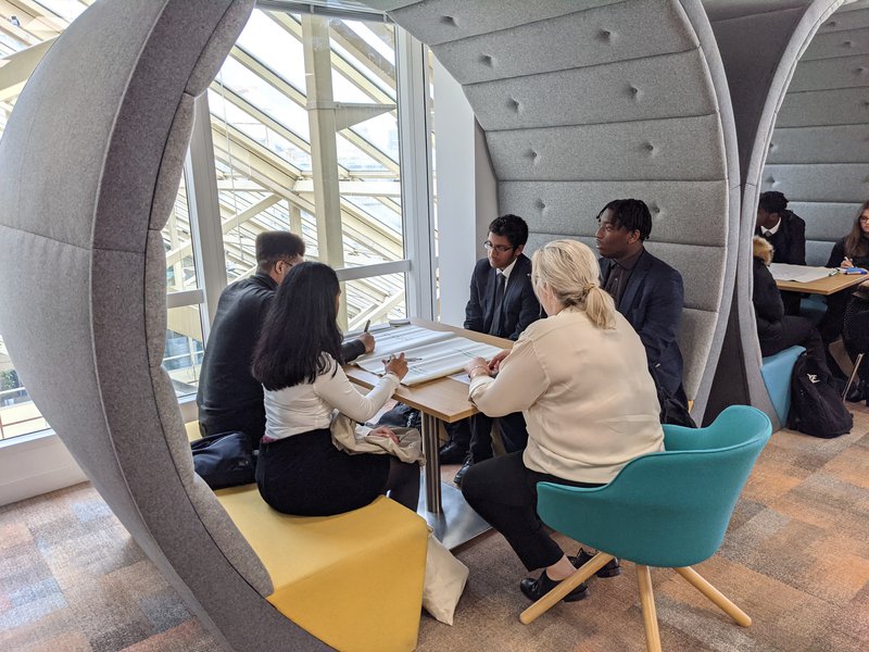 Long view of groups of students at Tideway work experience day, sitting in circular booths chatting together with a professional