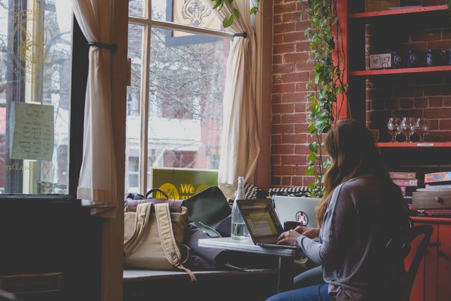 Picture of woman working on a laptop in a coffee shop window.